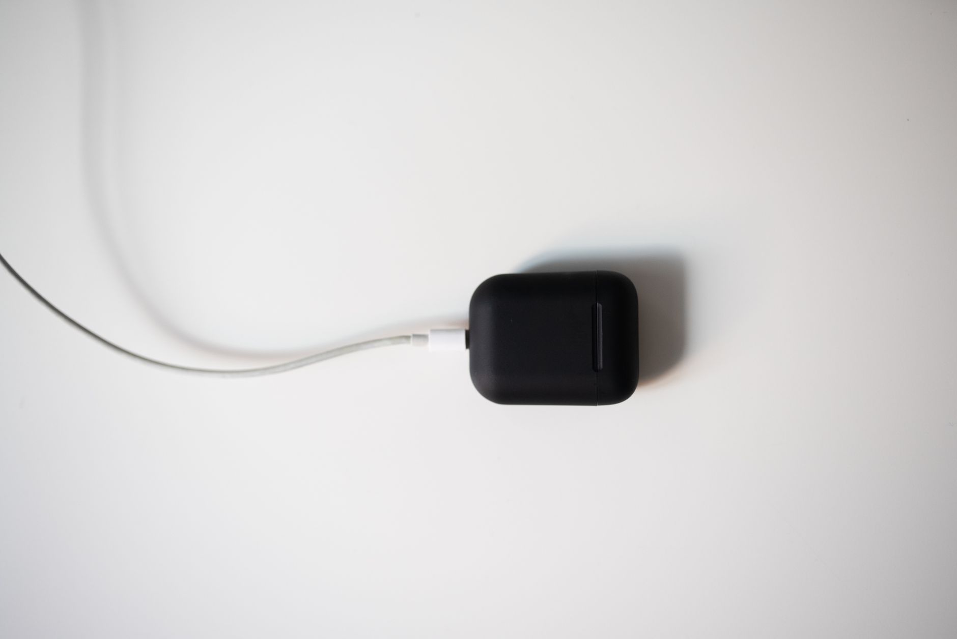 Apple AirPods Pro 2 and Sony WF-1000XM5 wireless earbuds charging cases sitting on a wooden desk next to a smartphone